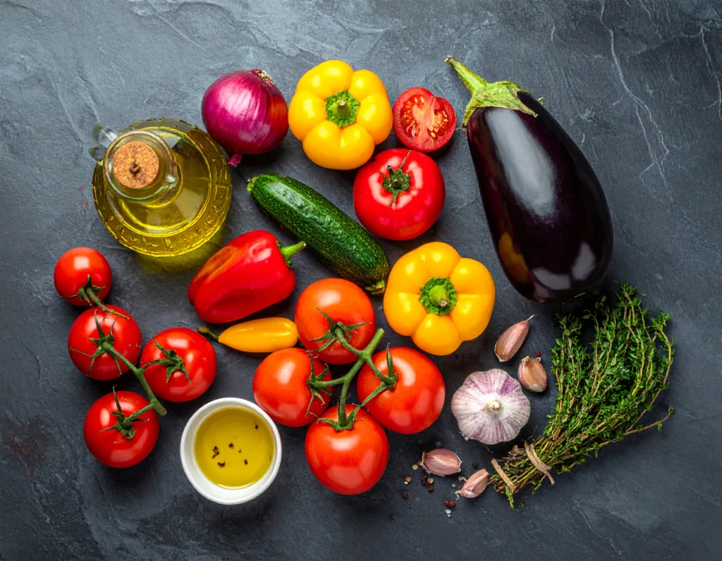 Présentation à plat des ingrédients ratatouille : aubergine, courgettes, poivrons, tomates, ail et oignon, prêts pour la recette ratatouille.