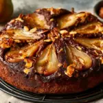 Gâteau poire chocolat amande entier sur une grille, poires en rosace et amandes effilées dorées